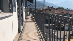 A balcony with a tiled floor, metal railing, and a view of a street with houses and mountains in the background.