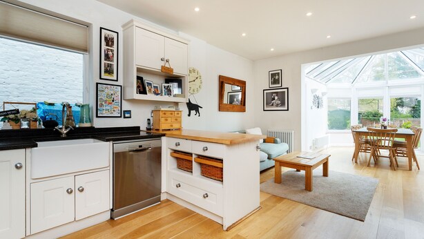 Una cucina moderna con mobili bianchi, un piano di lavoro in legno e una lavastoviglie integrata. C'è un'area pranzo con tavolo e sedie in legno, e un'ampia finestra che offre luce naturale.