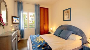 Une chambre à coucher avec un lit, une commode, un miroir, un téléviseur et une fenêtre avec des rideaux.