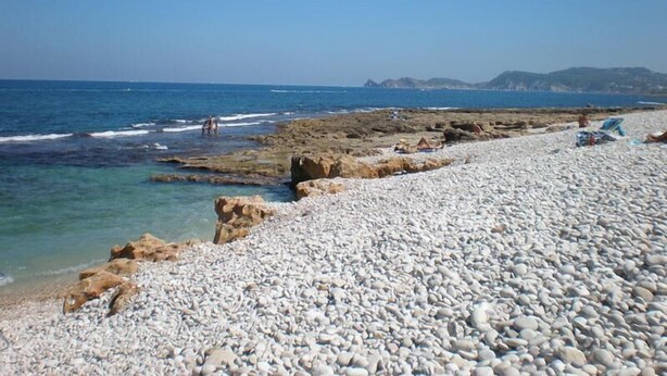 Une plage de galets avec des affleurements rocheux et une mer calme.