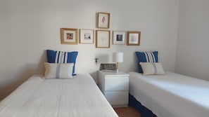 Une chambre d’hôtel avec deux lits simples, une table de chevet avec une lampe et un mur décoré de tableaux encadrés.