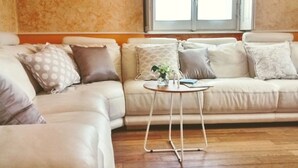 Een woonkamer met een beige bank, een ronde salontafel en een raam met jaloezieën.
