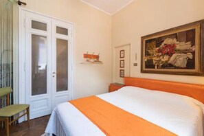 Een slaapkamer met een bed, een deur met gezandstraalde glaspanelen, een lijst met een schilderij en een kleine tafel.