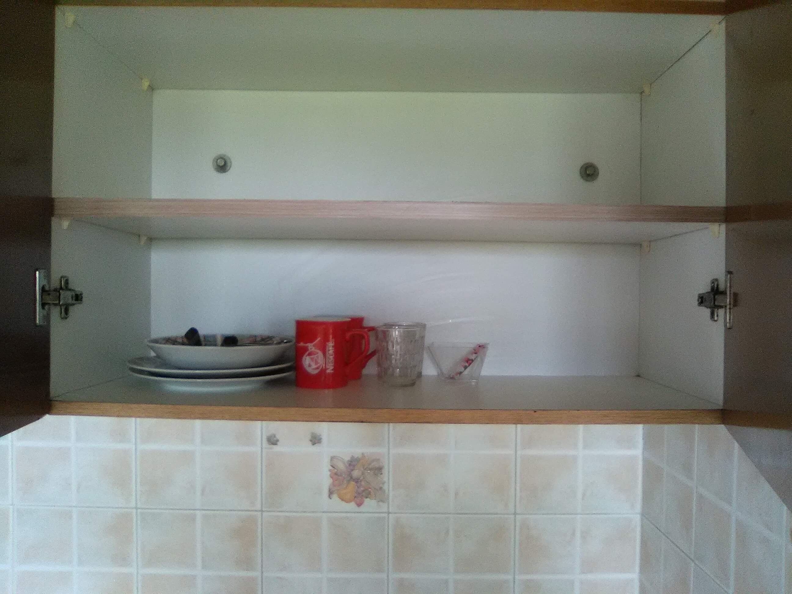 A kitchen with a double sink, a red mug, and a glass on the countertop.