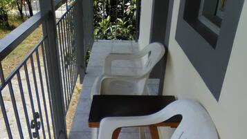 A balcony with two white plastic chairs and a small table, a metal railing, and a tiled floor.