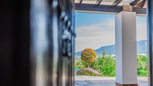 Vista a través de una puerta a un patio con montañas al fondo, destacando un árbol grande y diversas plantas.