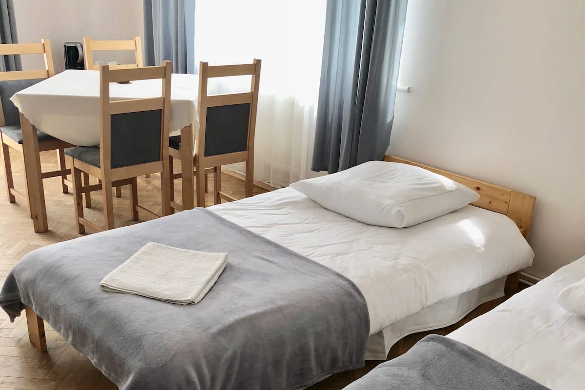 A hotel room with two single beds, a wooden table with chairs, and a large window with curtains.