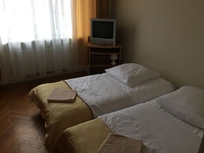 Ein Zimmer mit zwei Betten, einem Fernseher auf einem Schrank und einem fenster mit Vorhängen.