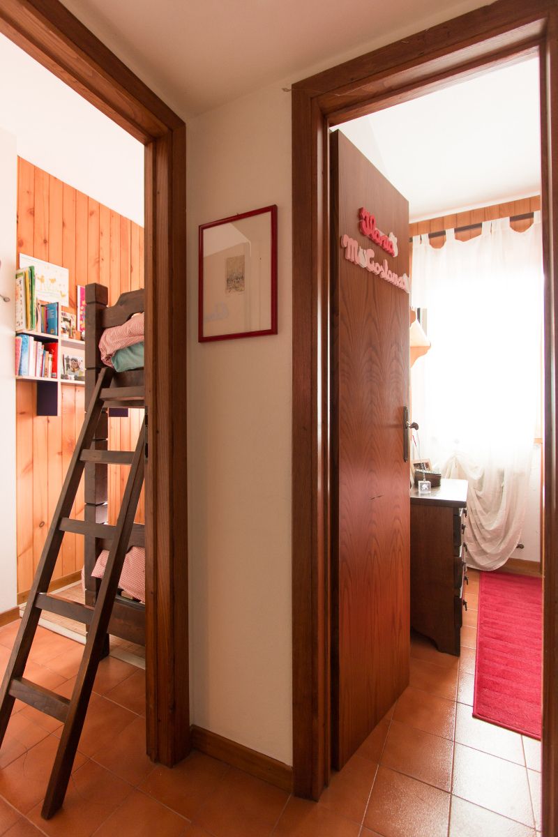 Une pièce avec une échelle en bois menant à un lit en mezzanine, un certificat encadré accroché au mur et une porte donnant sur une autre pièce dotée d’une moquette rouge.