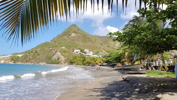 A beach with a mountain in the background, a boat on the shore, and a few people relaxing. - ❤T2 of standing, sea view, 2 minutes from beaches, quiet, nature, wifi, air conditioning (Les Anses-d'Arlet)