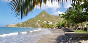 A beach with a mountain in the background, clear skies, and a few buildings.
