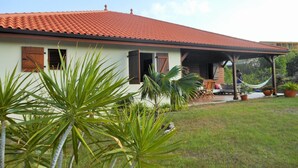 A house with a red tiled roof, a porch with a hammock, and a lawn with tropical plants. - ❤T2 of standing, sea view, 2 minutes from beaches, quiet, nature, wifi, air conditioning (Les Anses-d'Arlet)