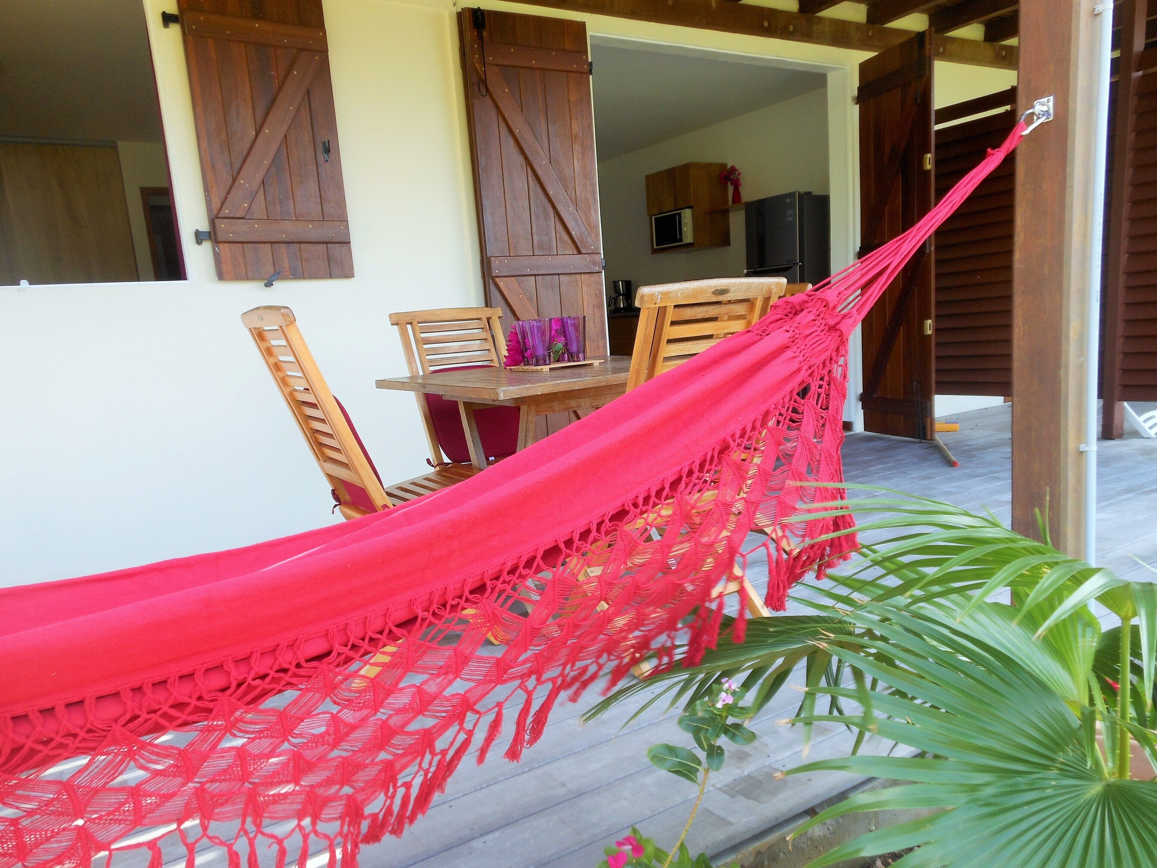A hammock tied between wooden chairs and a table, with a view of a kitchen and a door in the background.