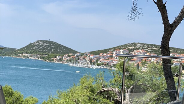 Un área de piscina con dos sillas de descanso y una mesa, con vistas a un pueblo costero y al mar.