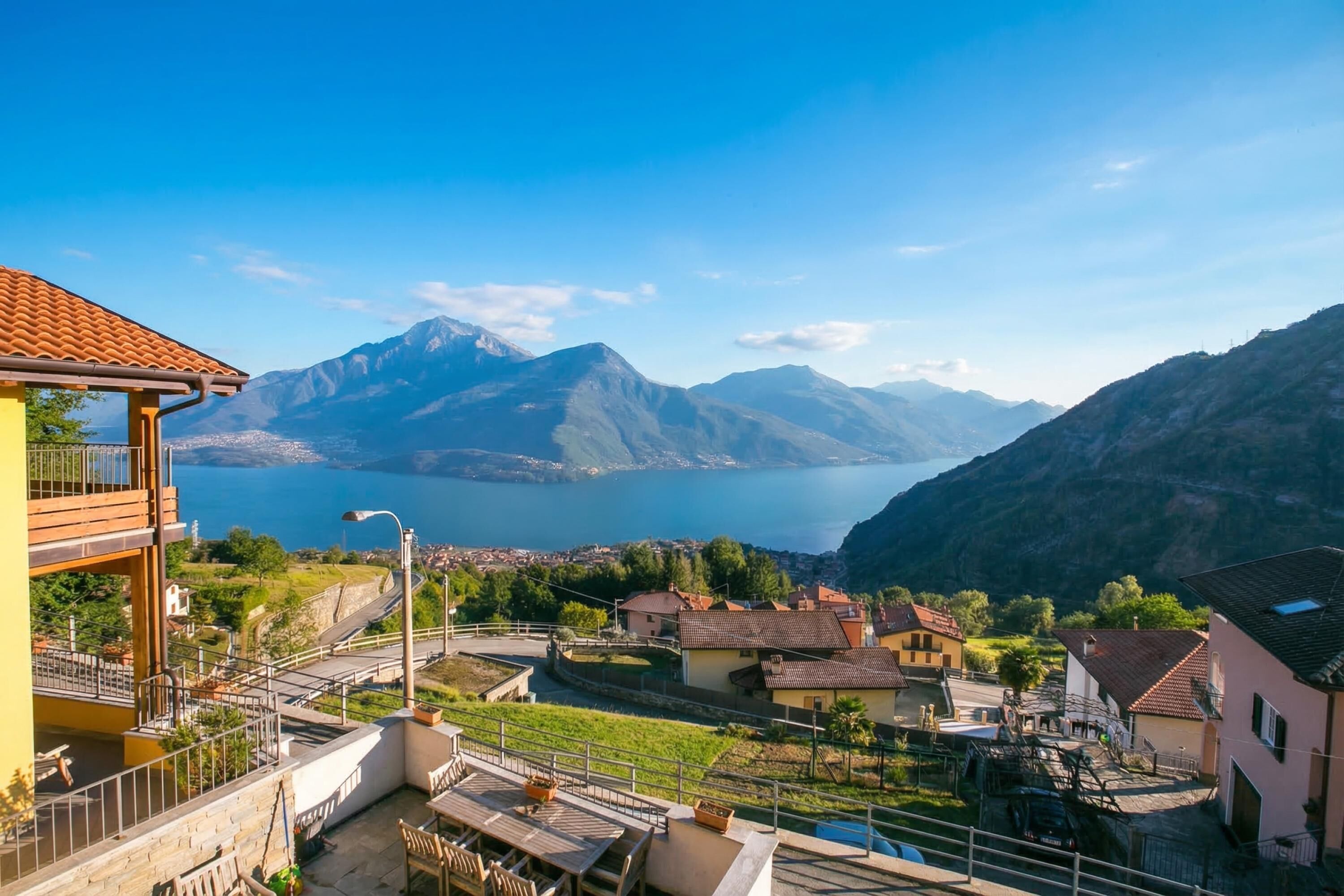 Ein Wohngebiet mit Blick auf Berge und einen See, mit Häusern mit roten Ziegeldächern und einem Balkon mit Gartenmöbeln.