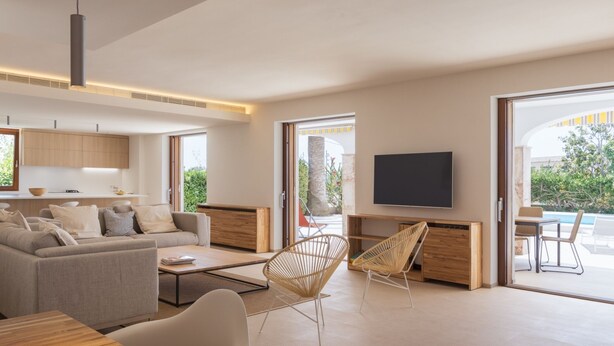 A modern living room with a sofa, coffee table, and chairs, a flat-screen TV mounted on the wall, and large windows offering a view of the outdoors. - Can Ribas - Spectacular villa with pool near Palma (Marratxi)