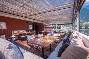 An outdoor dining area with multiple tables and chairs, a stone wall, and a view of a town and water.
