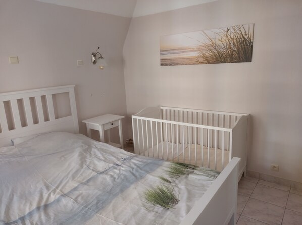 Un dormitorio con una cuna, una mesita de noche pequeña, una lámpara de pared y un cuadro con motivos playeros.