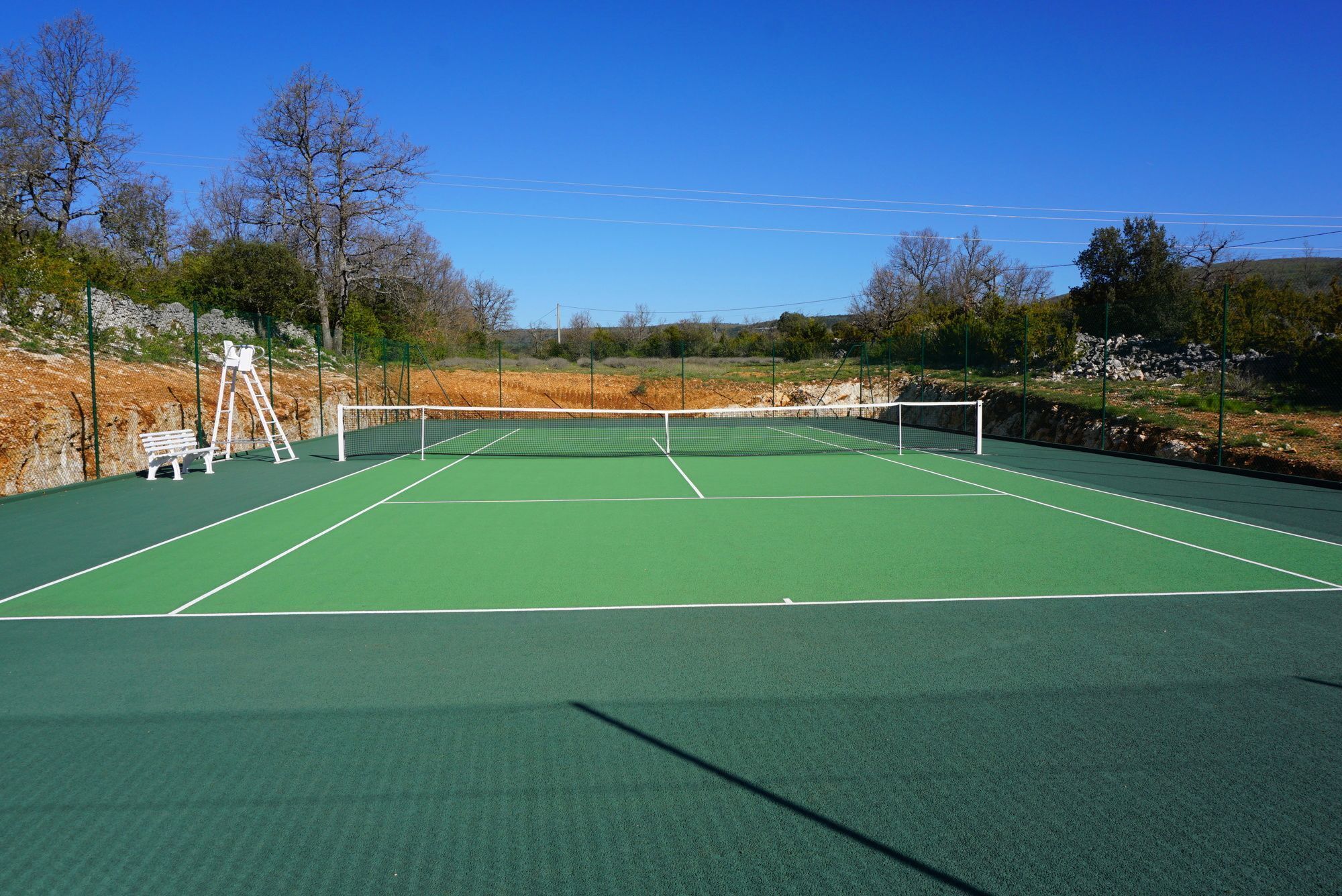 An outdoor tennis court with a net, benches, and a ladder.