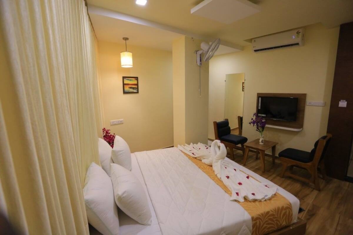 Quarto de hotel com cama, escrivaninha, cadeira, televisão e espelho.