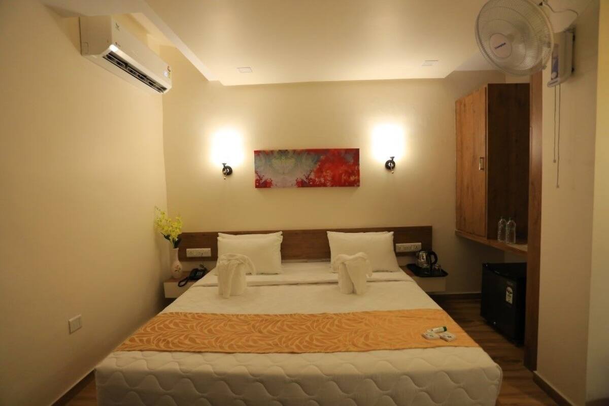Quarto de hotel com cama, mesa de cabeceira, abajur e uma obra de arte na parede.