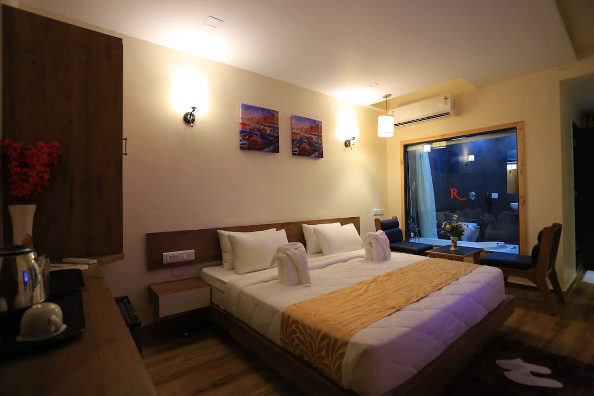 Quarto de hotel com uma cama grande, cabeceira de madeira, mesa de cabeceira com luminária, janela com vista e obras de arte na parede.