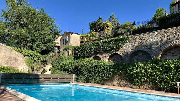 Une piscine aux murs en pierre et un pont également en pierre.
