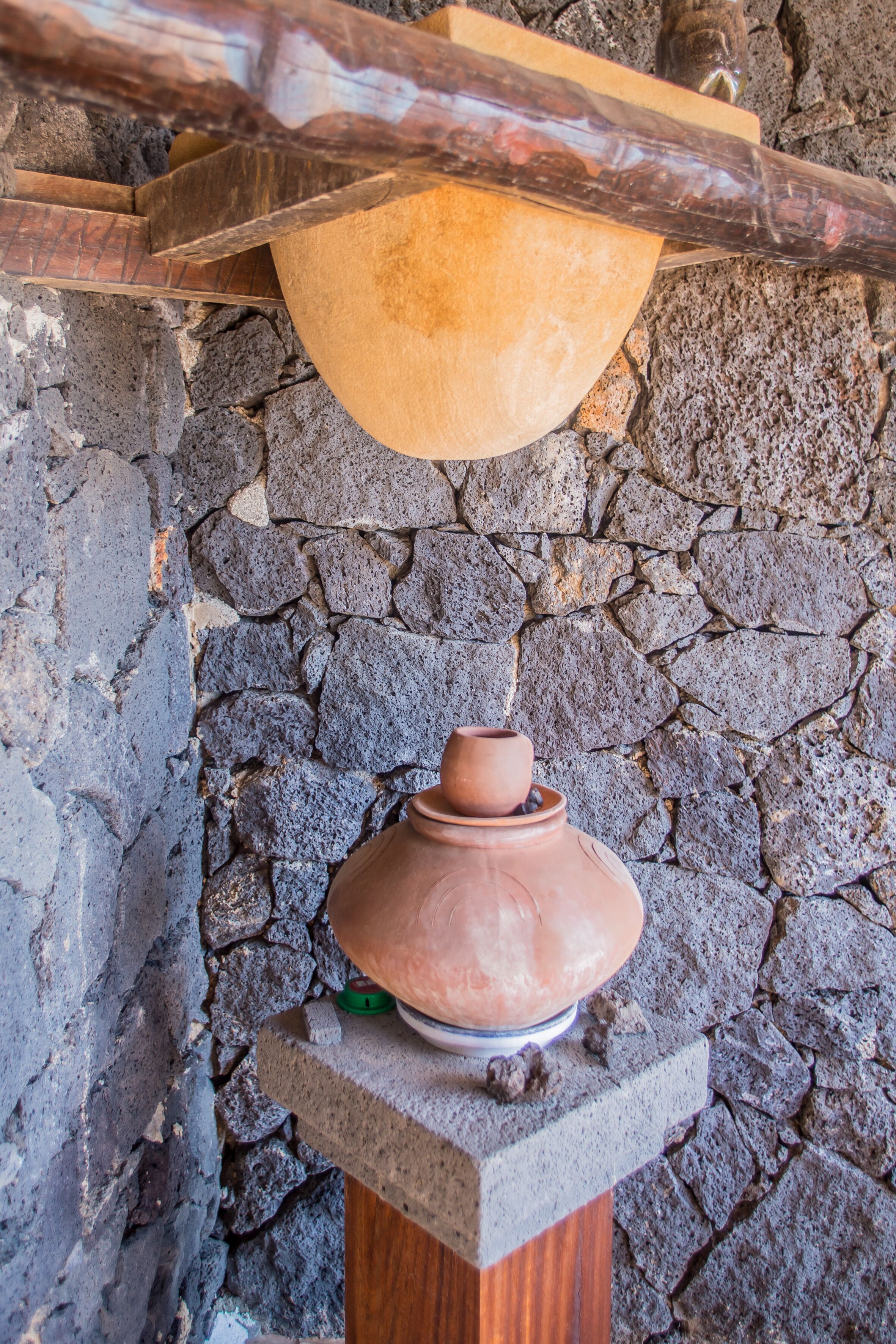 A clay pot on a pedestal against a stone wall.