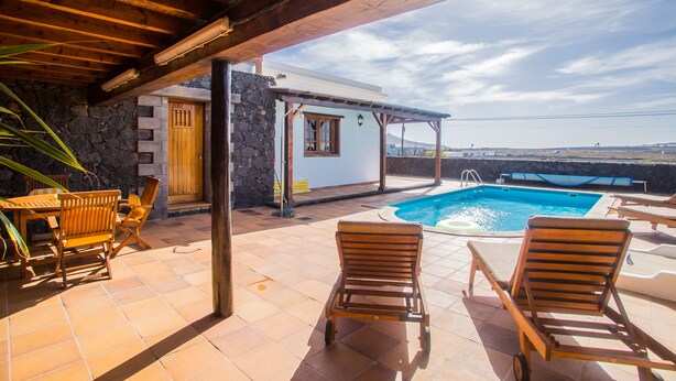 Ein Poolbereich mit Holzliegen, einer Steinmauer und einer überdachten Terrasse.