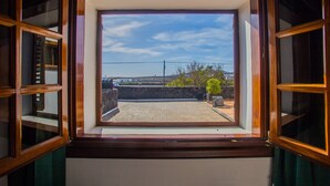 Ein Fenster mit Blick auf eine gepflasterte Fläche, eine Steinmauer und etwas Grün.