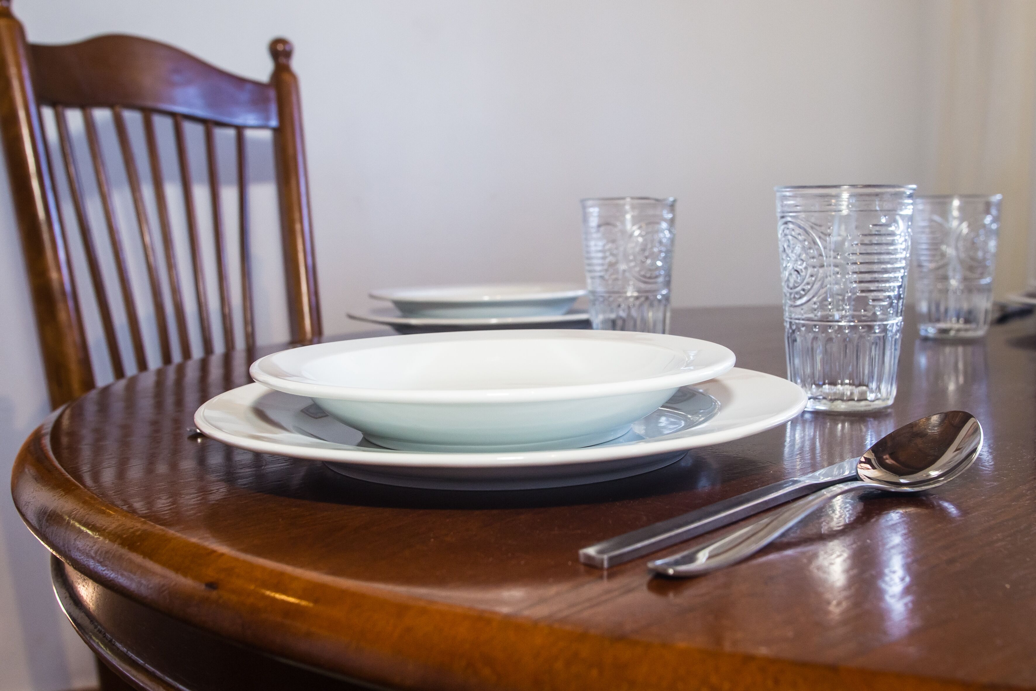 A dining table with a white plate, a spoon, and clear glasses.