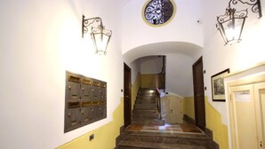 A staircase with a metal railing, a wall-mounted light fixture, and a door with a sign. - Convenient and cozy apartment in the heart of the city nearby historic center (Palermo)