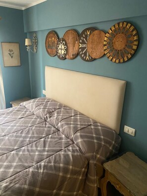 Une chambre à coucher comprenant un lit, une tête de lit, une table de chevet, une horloge murale et une lampe fixée au mur.