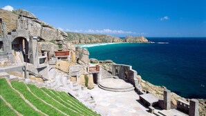 Una escalera de piedra conduce a una terraza con vistas a una zona costera de aguas azules cristalinas y una isla distante.