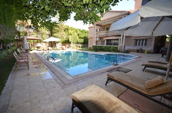 Une piscine avec des chaises longues, un espace de détente couvert et un bâtiment doté de balcons.