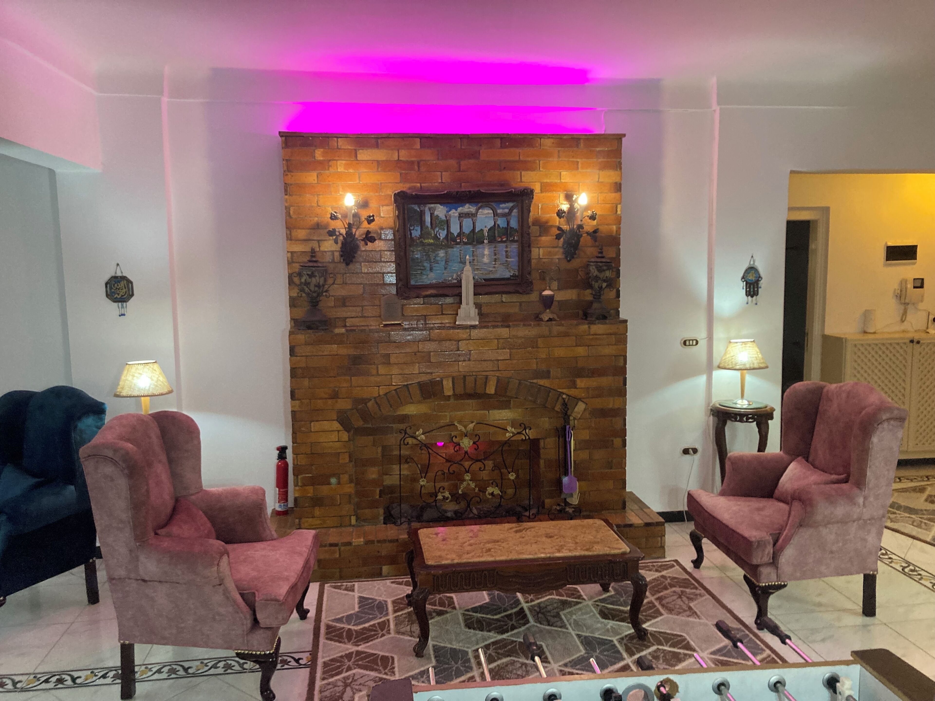 Un salon avec une cheminée en briques, deux fauteuils, une table basse et un tapis à motifs.