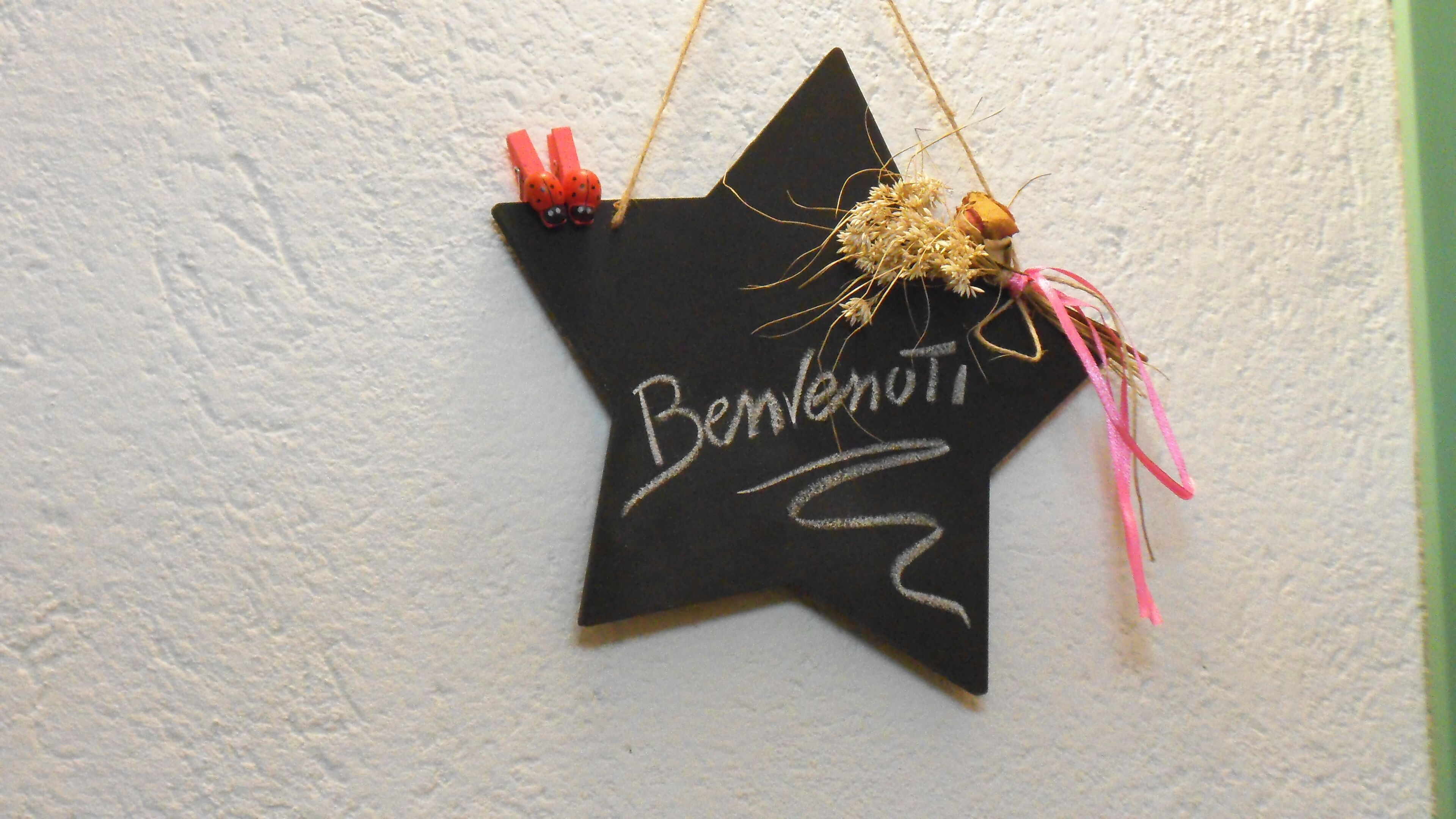 Une décoration noire en forme d’étoile, sur laquelle est inscrit le mot « Benvenuti », est suspendue à un mur texturé.