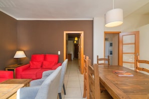 Una sala de estar con un sofá rojo, un sofá gris, una mesa de comedor de madera y una lámpara.