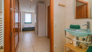 A hotel room with a glass sink, wooden door, tiled floor, and a bed with a gray bedspread. - Rural house Montseny, Cal Metge (GUALBA)