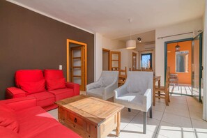 A living room with a red sofa, a wooden coffee table, and two white armchairs.