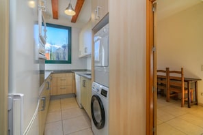 Una cocina funcional con lavadora, horno integrado y comedor con mesa y sillas de madera.