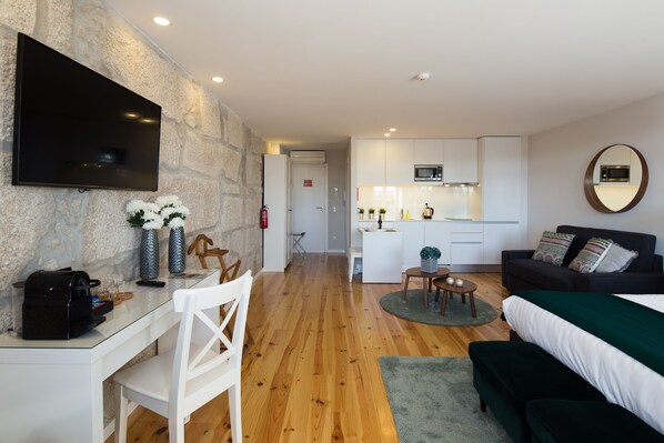 Una sala moderna con televisor, un comedor con mesa y sillas, una cocina con armarios blancos y un microondas, y una zona de descanso acogedora con una manta verde.