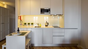 Una cocina moderna con muebles blancos, un microondas de acero inoxidable y una pequeña isla con una botella de vino.