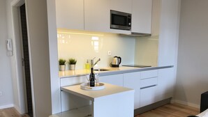 Cocina compacta con armarios blancos, microondas, lavabo y un pequeño comedor con banco.