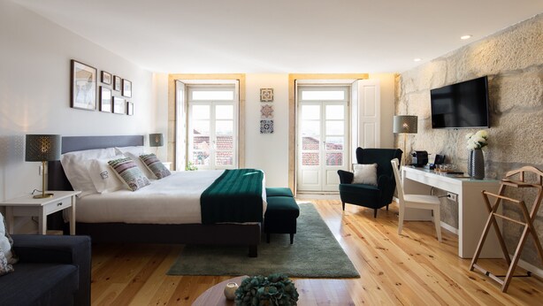 Un dormitorio moderno con cama, mesitas de noche, un escritorio, una silla, un televisor y vistas a través de la puerta.