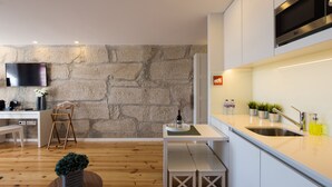 Una cocina moderna con armarios blancos, pared de piedra, horno empotrado y zona de comedor de madera.