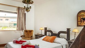A hotel room with a bed, a chair, a nightstand, a lamp, a window with curtains, and a poster on the wall.