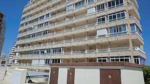 Un hôtel à plusieurs étages, doté de balcons à chaque niveau, d’une façade sobre et d’une entrée sécurisée par un portail.