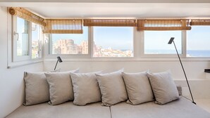 A room with a sofa, large windows with bamboo blinds, and a view of a cityscape. - Romantic Gem in Graça (Lisboa)