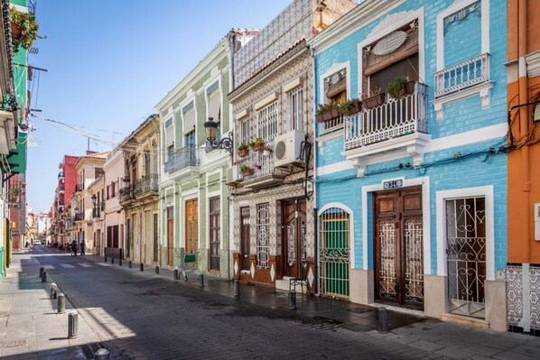 A street lined with colorful buildings, each with distinct architectural styles and balconies with potted plants.